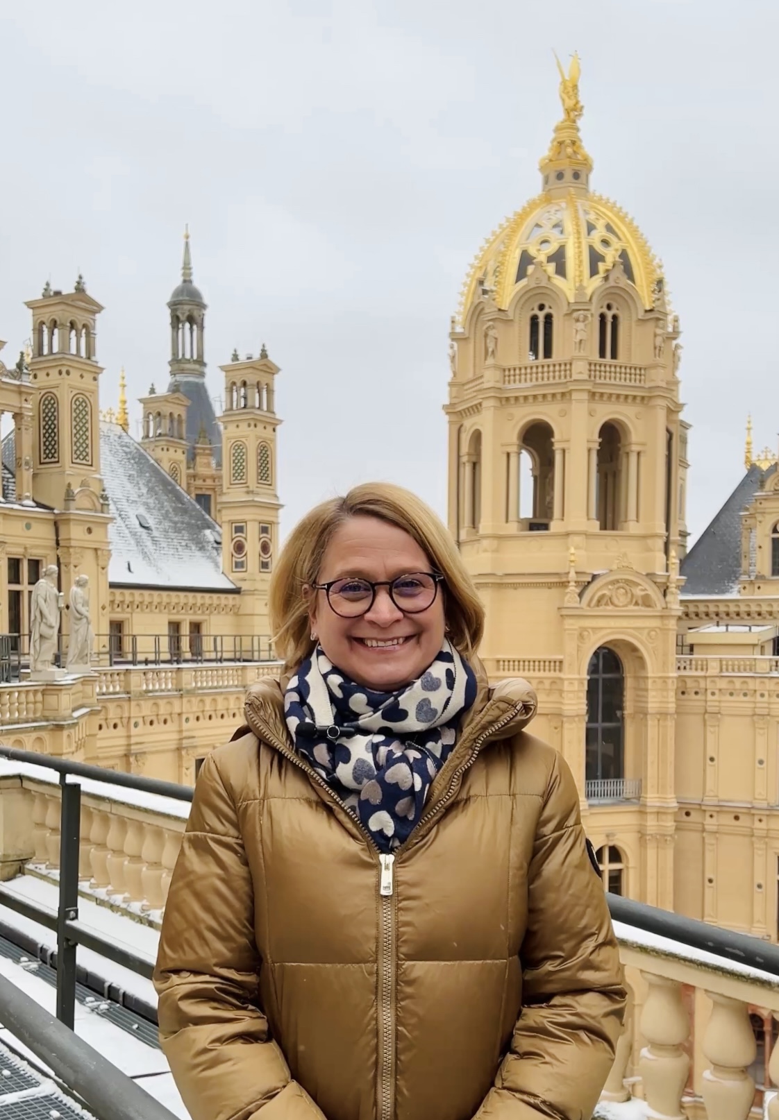 Frau in Winterjacke steht auf dem Dach eines Schlosses