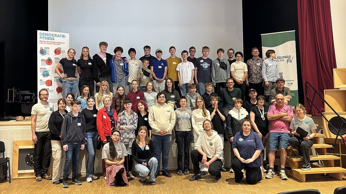 Gruppenbild von Jugendlichen vor einer Bühne in einem Saal