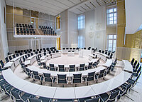 Moderner Plenarsaal des Landtags Mecklenburg-Vorpommern mit weißen Tischen und schwarzen Stühlen in halbrunder Anordnung