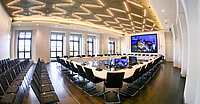 Moderner, heller Konferenzraum im Demmler-Saal des Landtags Mecklenburg-Vorpommern mit u-förmig angeordneten Tischen, Mikrofonen und Monitoren, umgeben von Stuhlreihen und großen Fenstern. Eine große Leinwand zeigt das Schweriner Schloss.