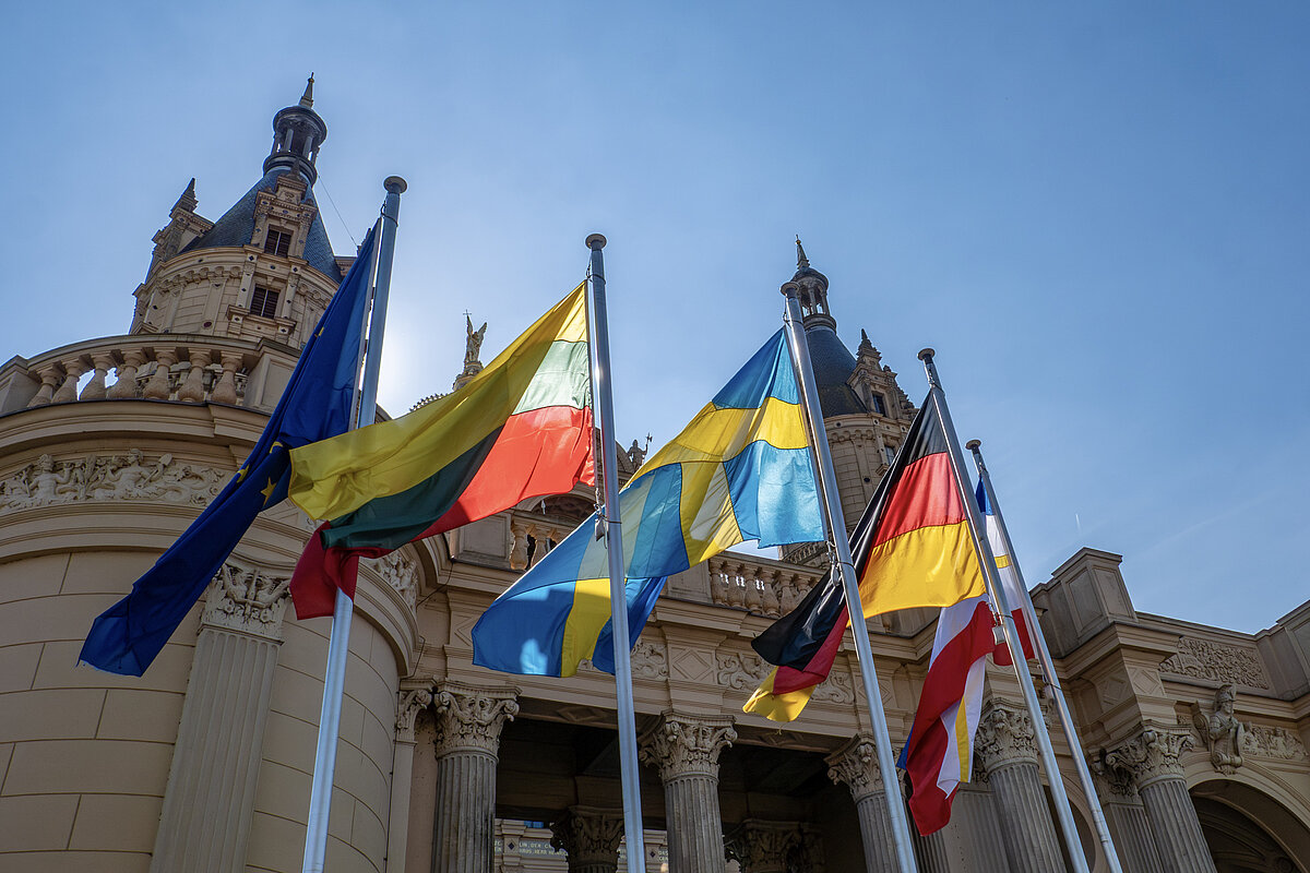 Die Flaggen von Europa, Deutschland, Schweden, Litauen und MV wehen vor einem historischen Schloss an einem sonnigen Tag
