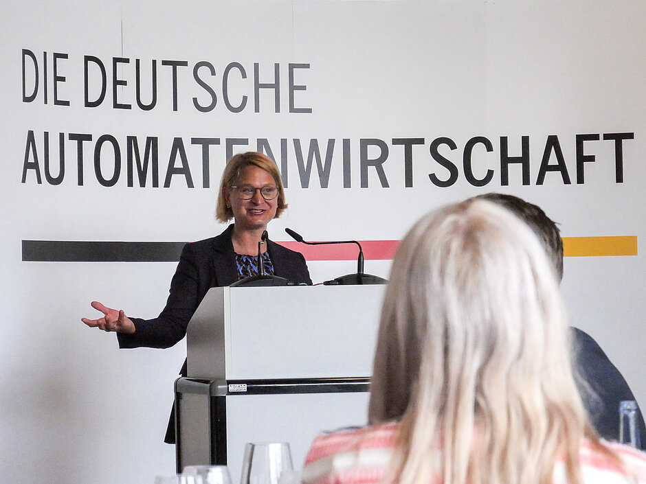 Landtagspräsidentin Birgit Hesse spricht lächelnd am Rednerpult vor dem Banner „Die Deutsche Automatenwirtschaft“ 