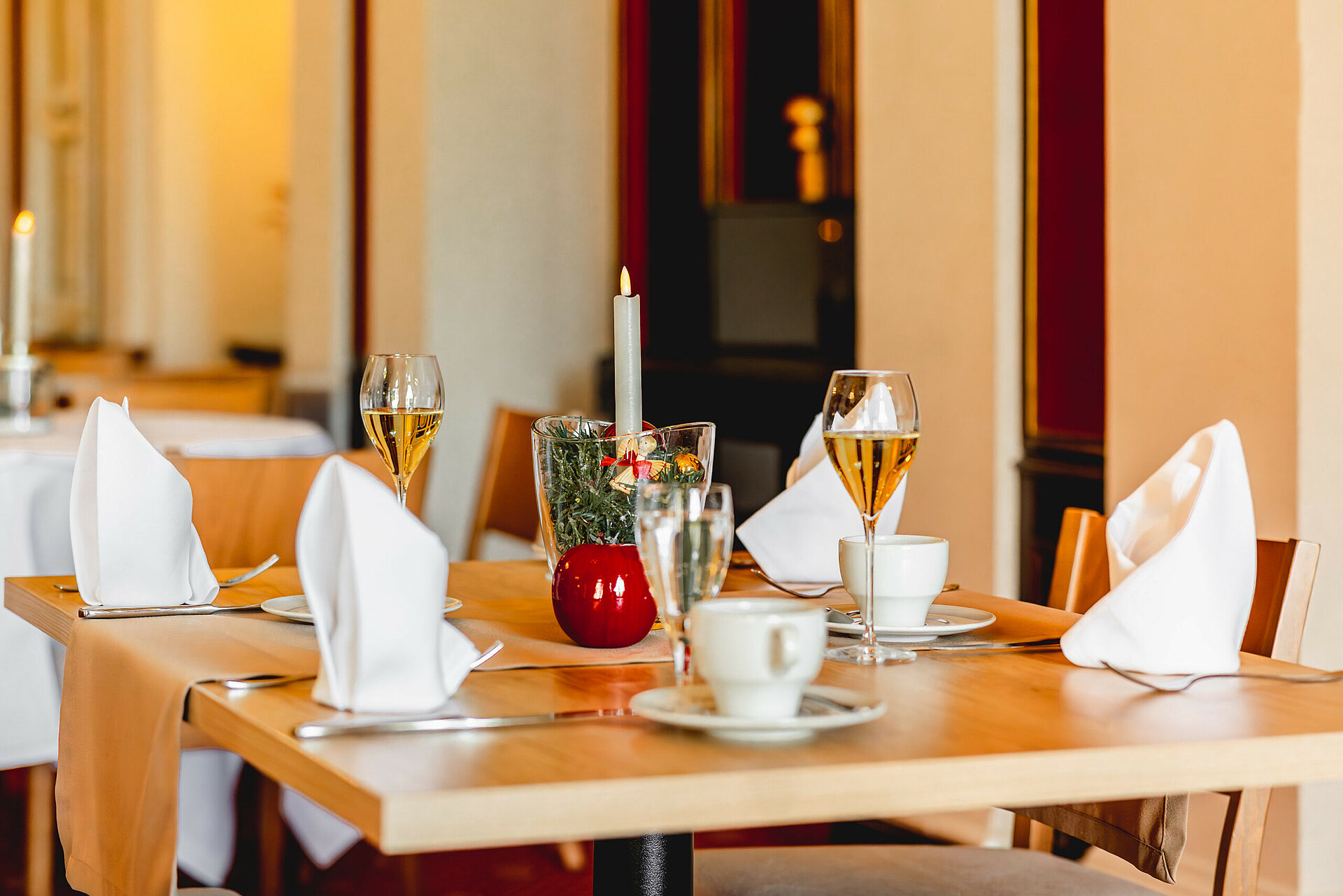 Ein liebevoll gedeckter Tisch für zwei Personen mit weißer Tischwäsche, Gläsern mit Sekt, einer brennenden Kerze und einer festlichen Dekoration.