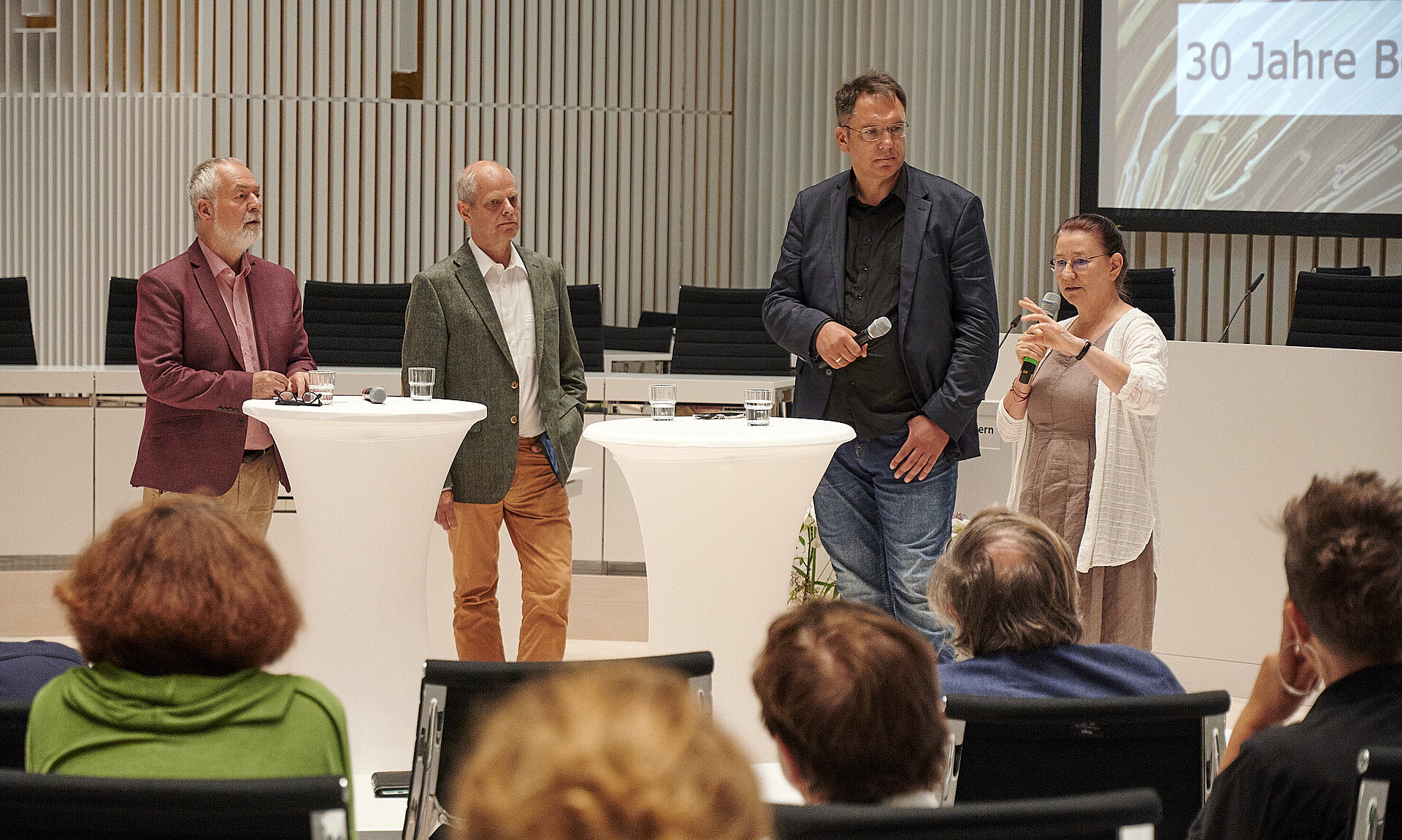 Vier Personen stehen bei einem Schlossgespräch im Plenarsaal des Landtages Mecklenburg-Vorpommern an zwei weißen Stehtischen und diskutieren vor Publikum. 