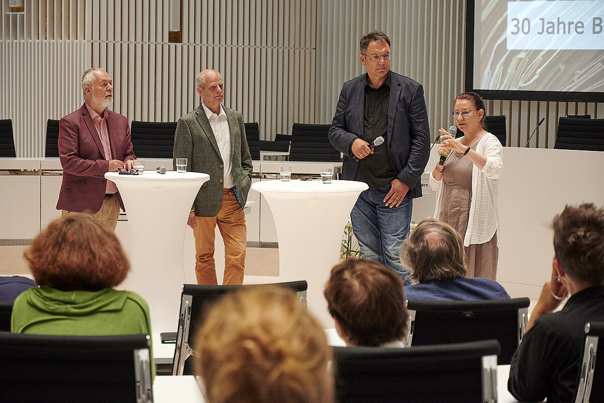 Vier Personen stehen bei einem Schlossgespräch im Plenarsaal des Landtages Mecklenburg-Vorpommern an zwei weißen Stehtischen und diskutieren vor Publikum. 