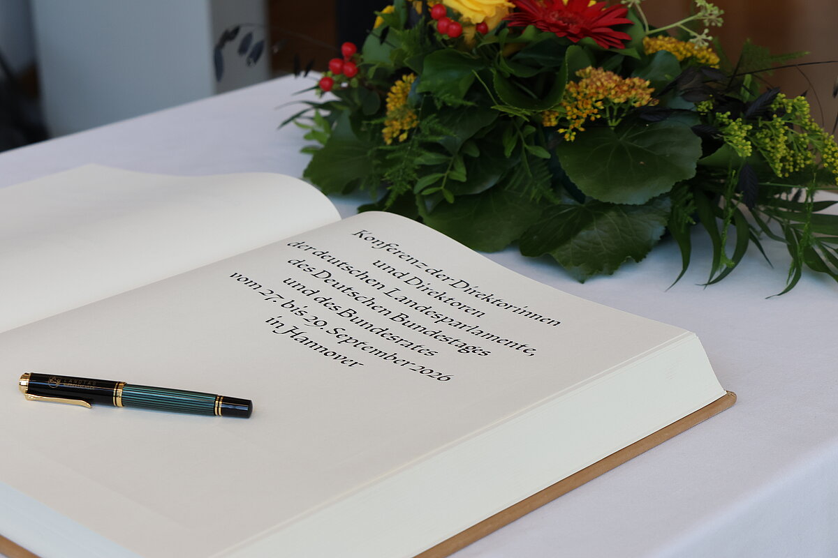 Ein Gästebuch mit Kalligrafie-Schriftzug liegt auf einem mit Blumen geschmückten Tisch
