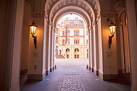 Blick durch einen beleuchteten Torbogen mit kunstvoll verzierten Säulen und Decken auf den Innenhof des Schweriner Schlosses mit historischer Fassade im Hintergrund.