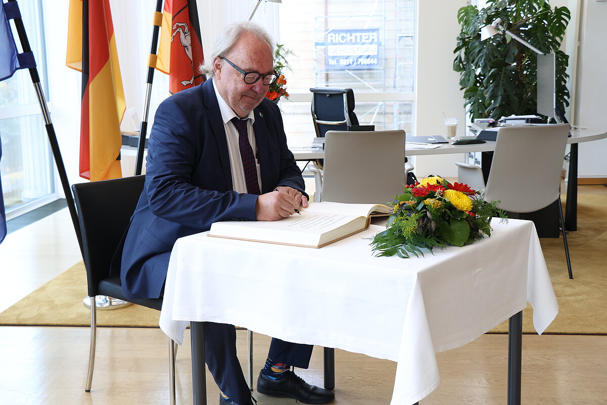 Landtagsdirektor im dunkelblauen Anzug sitzt am Tisch und trägt sich ins Gästebuch ein