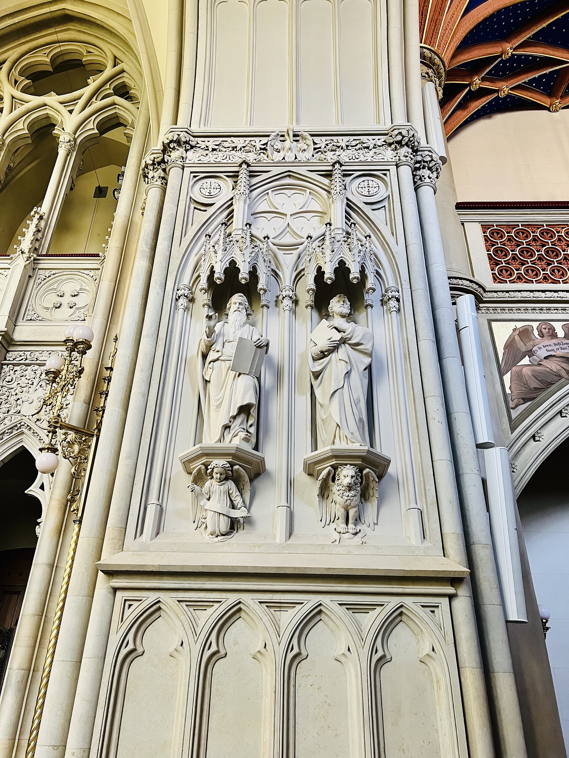 Detailaufnahme eines gotischen Wandreliefs in der Schlosskirche mit zwei Heiligenfiguren und symbolischen Tierdarstellungen darunter, eingerahmt von aufwendig verzierten Pfeilern.