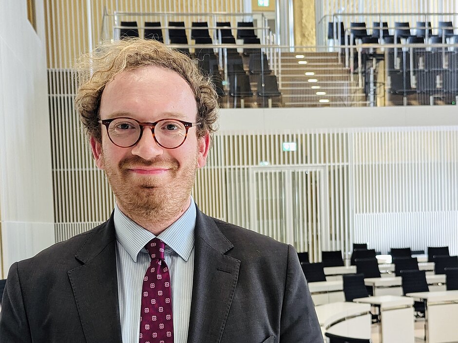 Ein Mann mit Brille und Anzug steht im Plenarsaal des Landtages Mecklenburg-Vorpommern und lächelt in die Kamera.