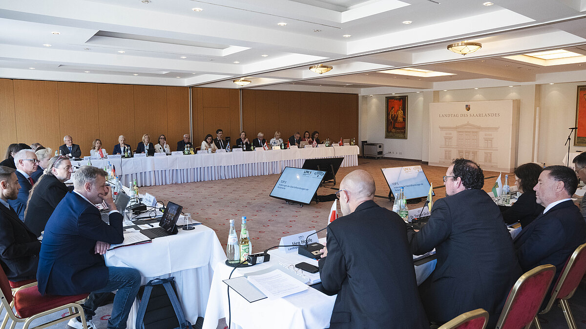 Konferenzraum mit mehreren Personen, die an einem U-förmigen Tisch sitzen und an einer Besprechung teilnehmen