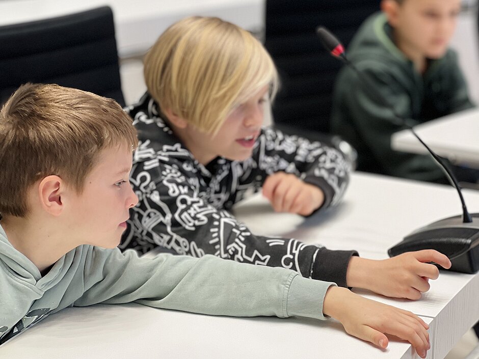 Schüler einer Besuchergruppe sitzen auf den Sitzen der Abgeordneten und betätigen ein Mikrofon