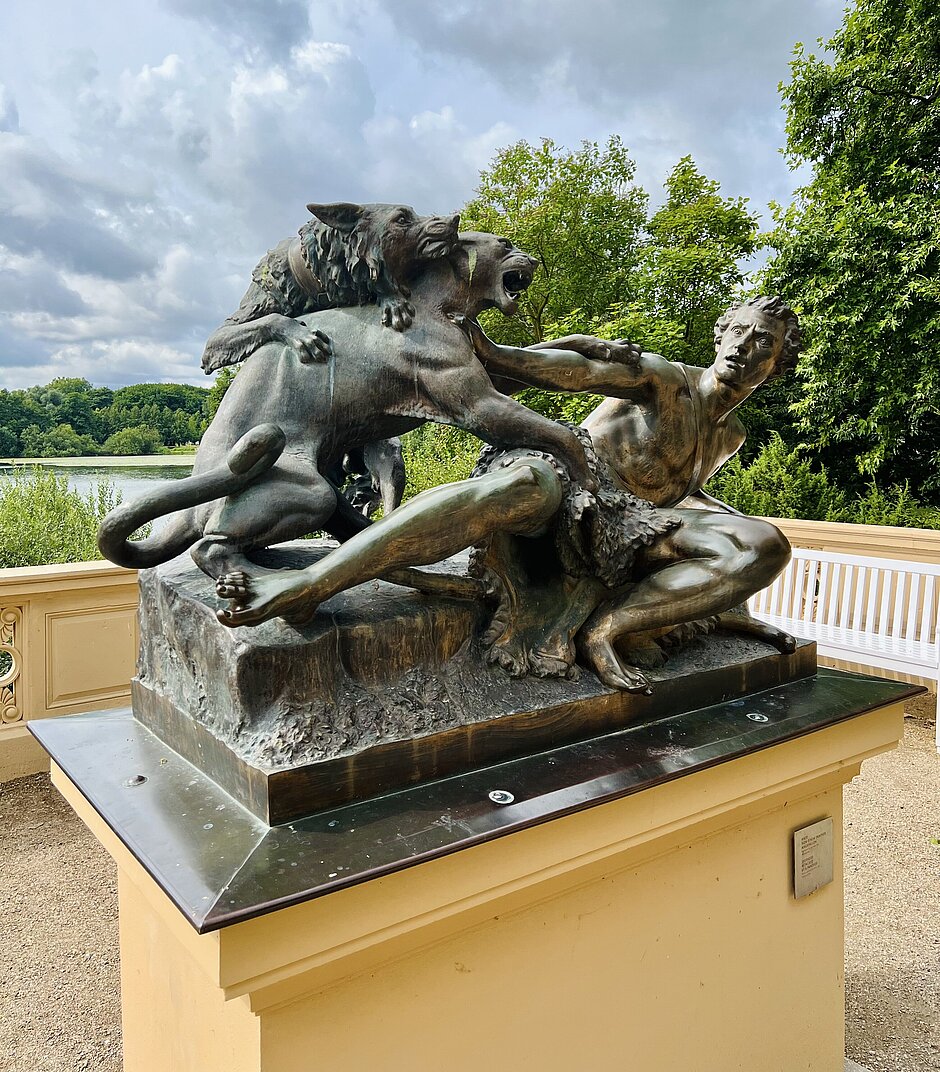 Bronzeskulptur eines kämpfenden Mannes mit zwei angreifenden Raubtieren, aufgestellt auf einem Sockel im Burggarten des Schweriner Schlosses