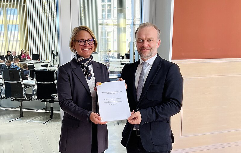 Landtagspräsidentin und Bürgerbeauftragter vor dem Plenarsaal halten gemeinsam den Jahresbericht während der Übergabe