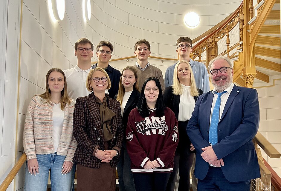 Fünf junge Männer und eine Frau in einem türkisfarbenen Anzug, stehen vor einem großformatigen historischen Gemälde im Schweriner Schloss und blicken in die Kamera.