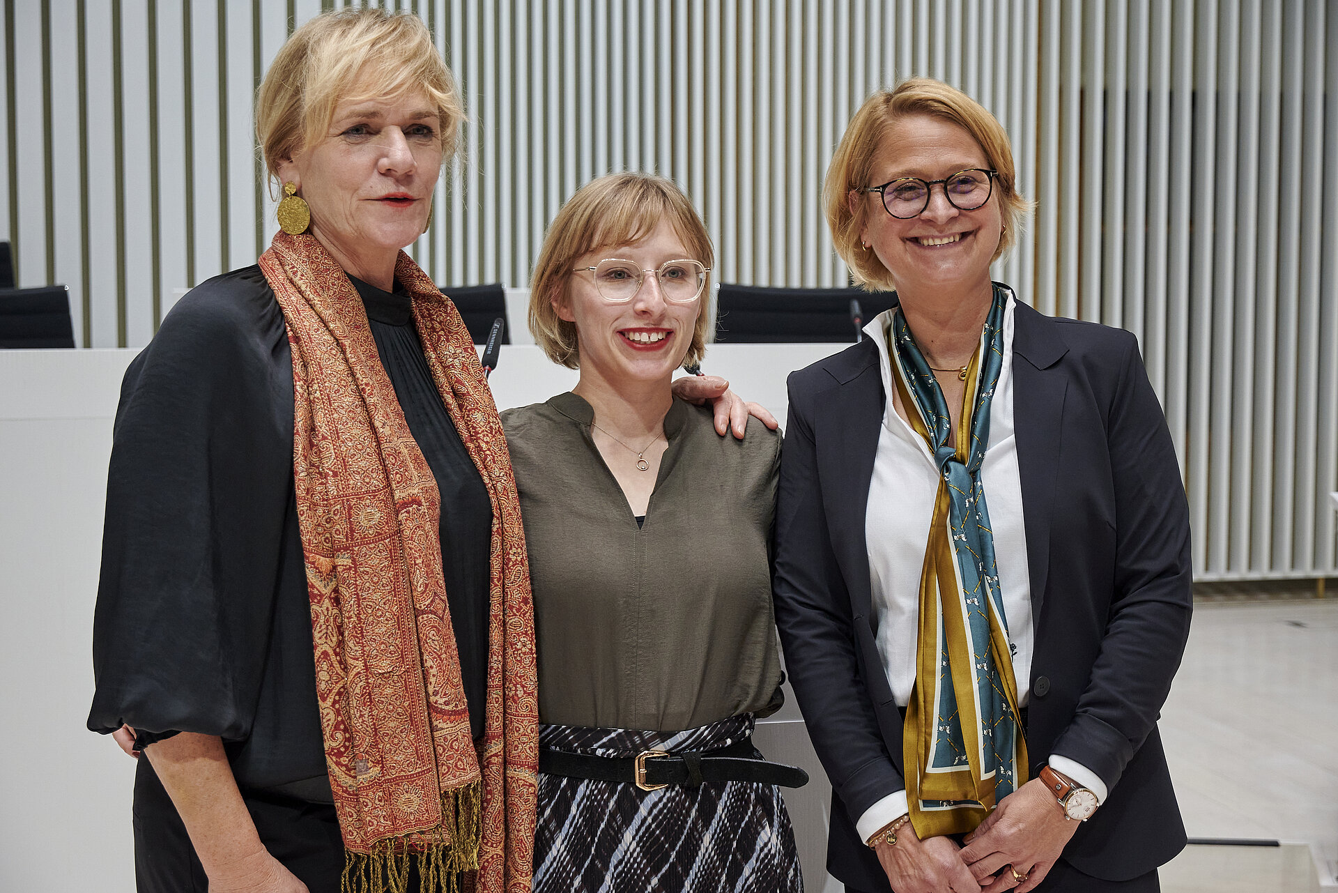 Drei Frauen stehen im Plenarsaal des Landtages und lächeln dem Publikum zu